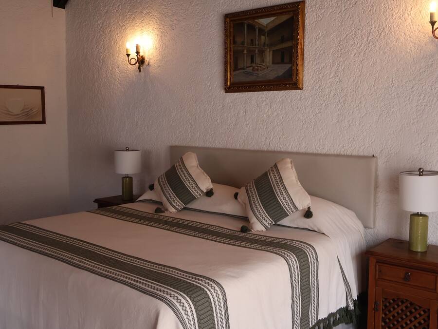 Una cama bien hecha con una colcha estampada, dos lámparas de noche y una mesita de noche de madera con un cajón.