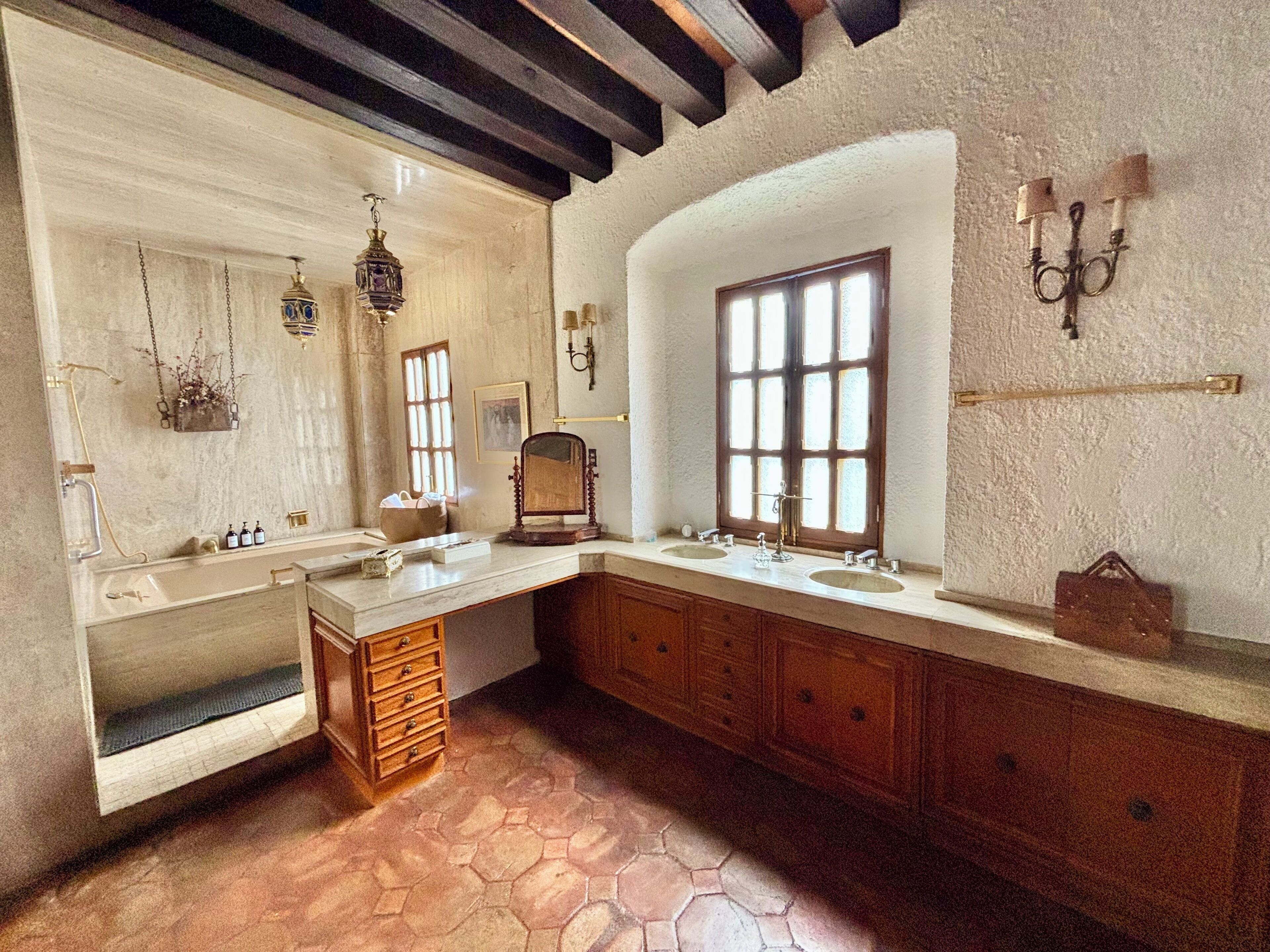 A bathroom with a large window, wooden cabinets, a mirror, and a sink.