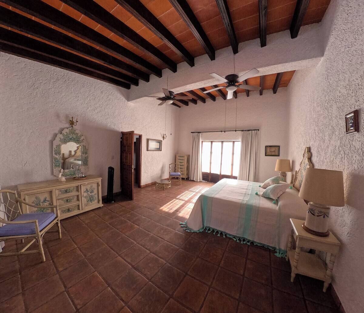 A spacious bedroom with a large bed, two ceiling fans, a dresser, and a chair.