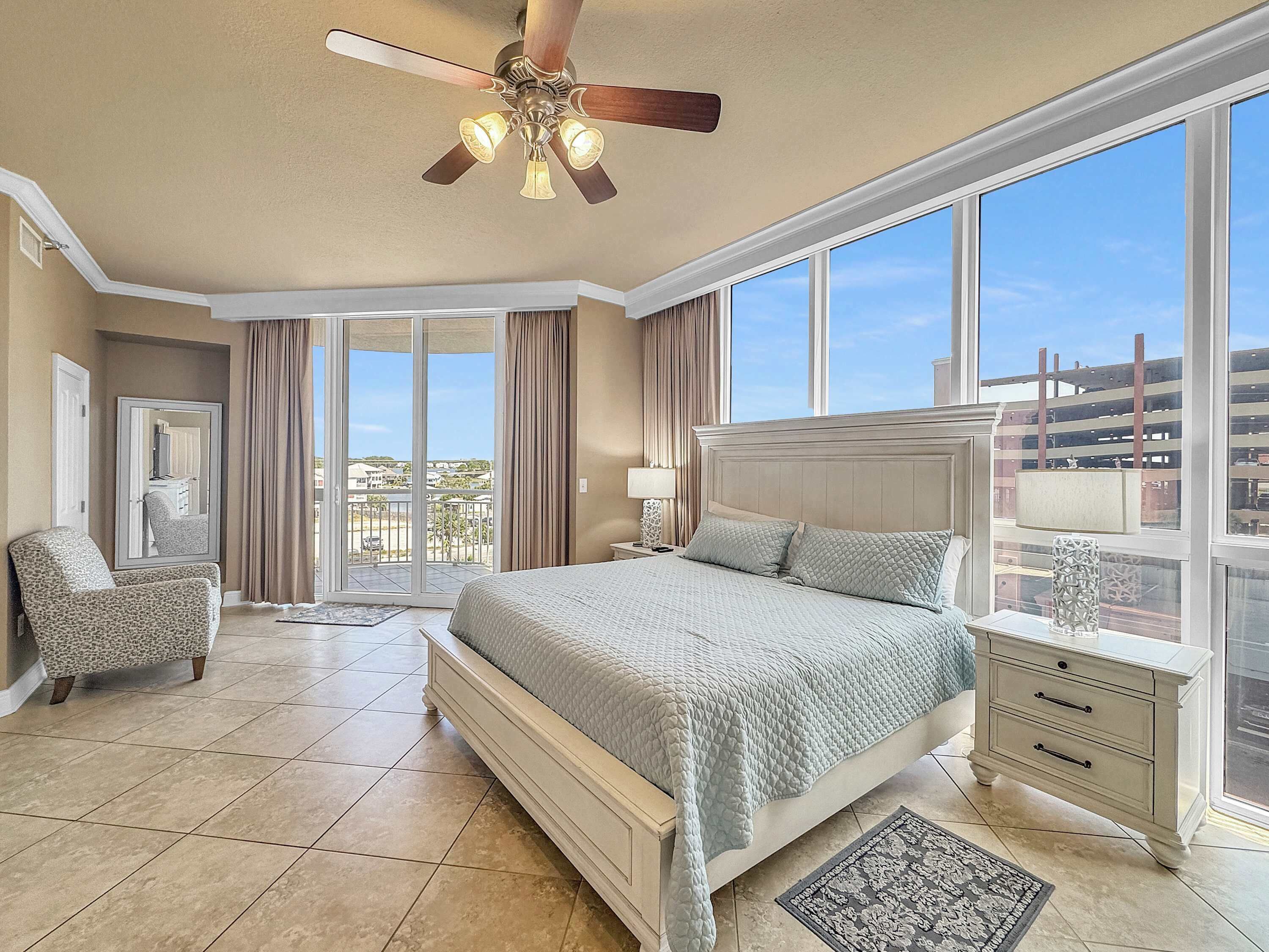 A spacious bedroom with a large bed, a ceiling fan, and a view of the city through large windows.