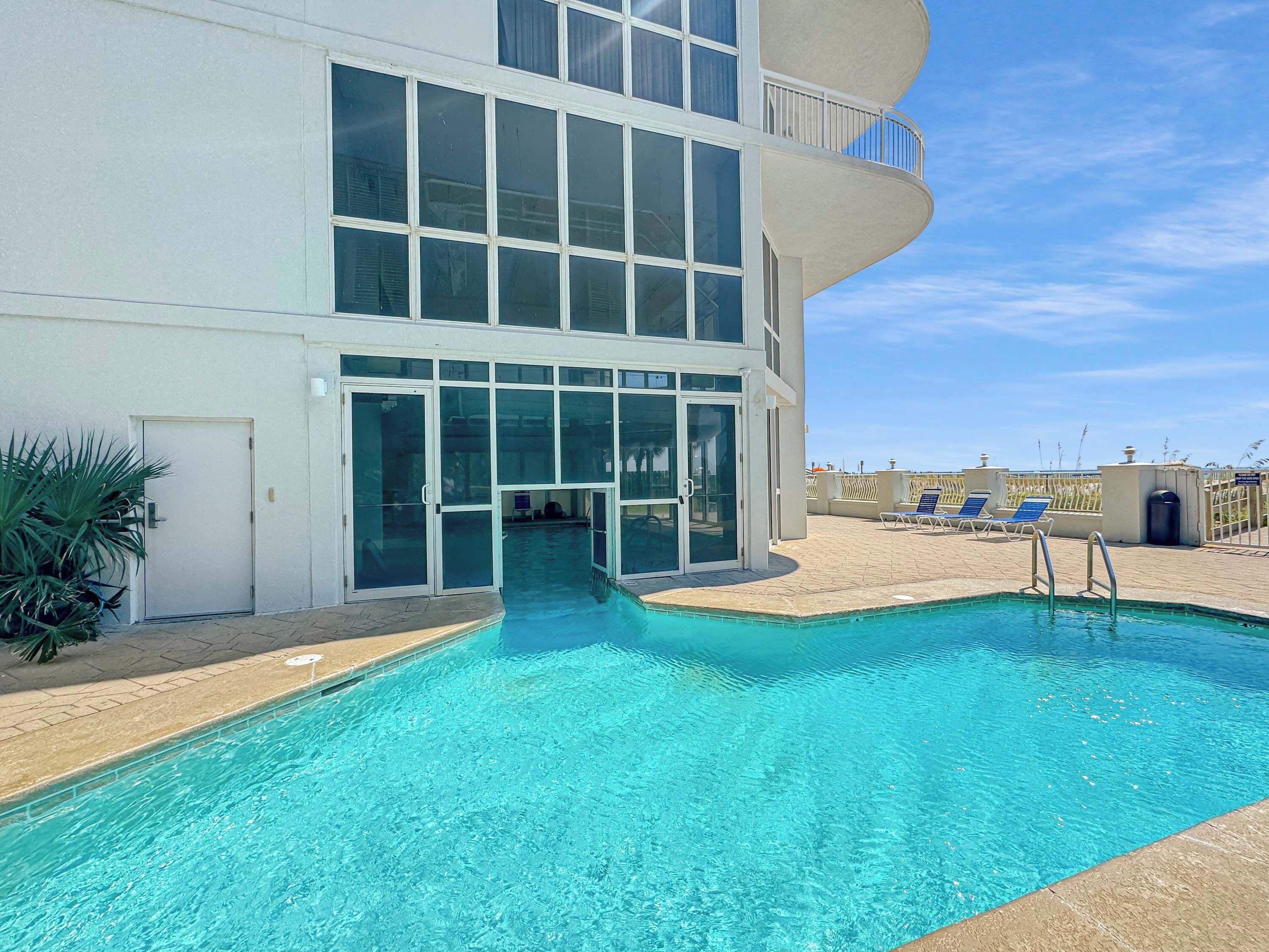 Un edifici modern amb piscina, grans portes de vidre i un balcó amb gandules.