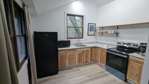 A modern kitchen with wooden cabinets, a black refrigerator, a microwave, a sink, and a stove.