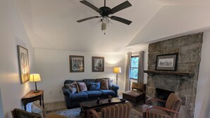 A living room with a stone fireplace, a ceiling fan, a blue sofa, and striped chairs.