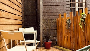 Eine Holzterrasse mit einem weißen Tisch und Stühlen, einem roten Blumentopf und einem Holzzaun.