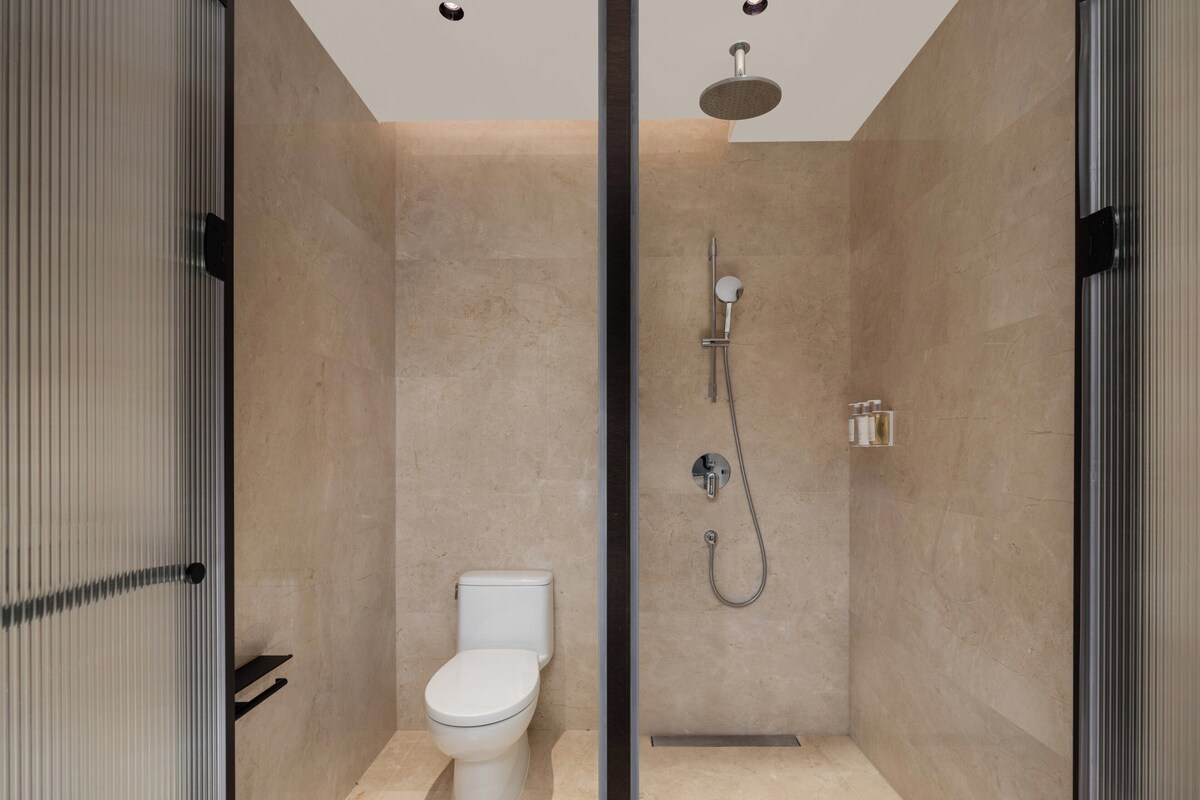 A modern bathroom with a toilet, a shower with a handheld showerhead, and a glass partition.