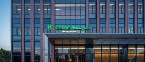 A modern hotel building with a glass facade, a prominent signage, and a well-lit entrance.