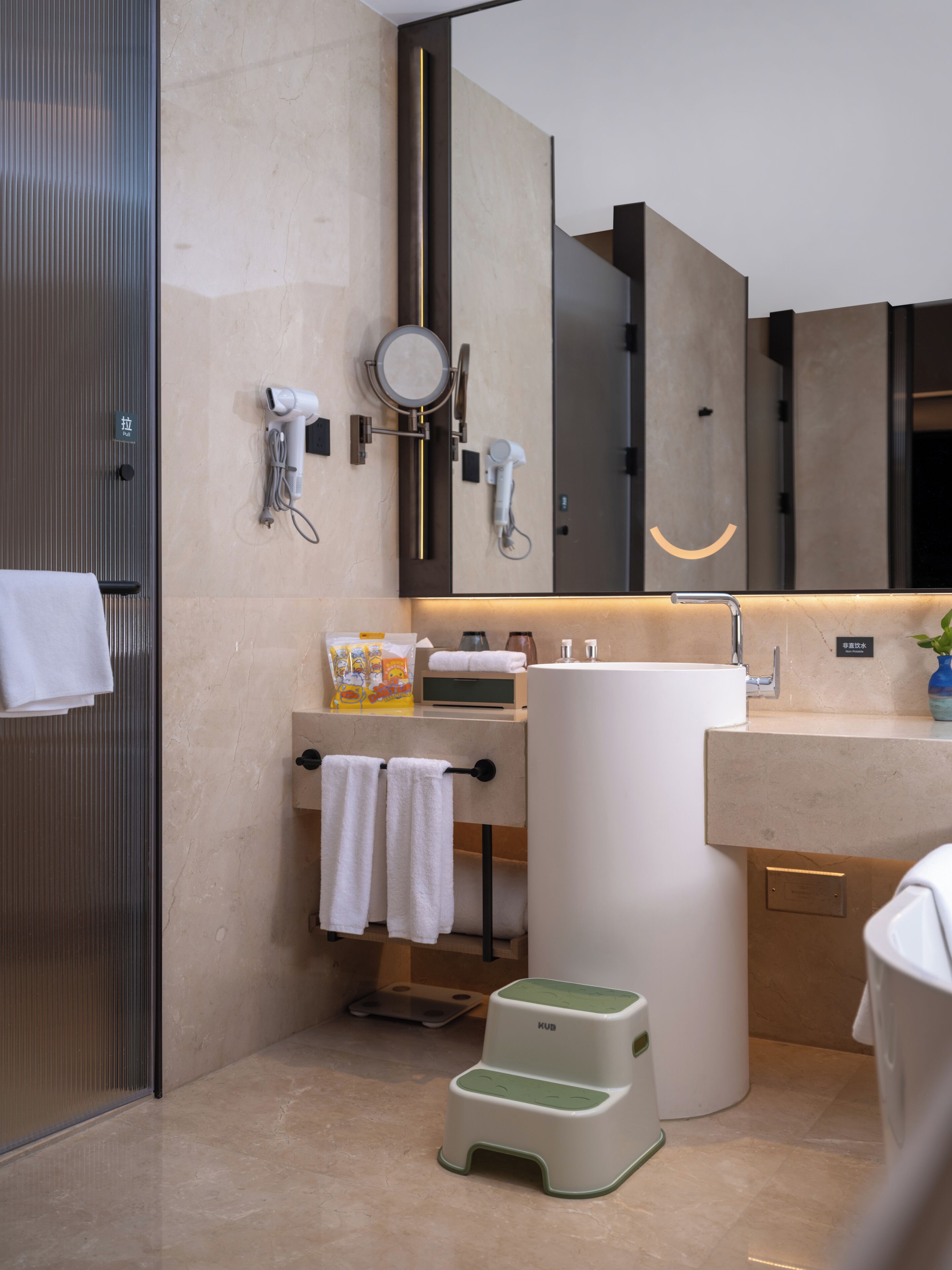 Un baño moderno con un espejo grande, un lavamanos, un perchero para toallas y un taburete.