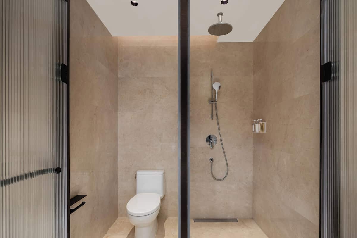 A modern bathroom with a toilet, a shower with a handheld showerhead, and a glass partition.