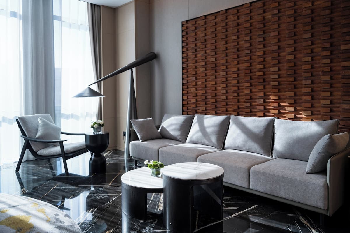 A modern living room with a sectional sofa, a round coffee table, a side table, a floor lamp, and a brick-patterned accent wall.