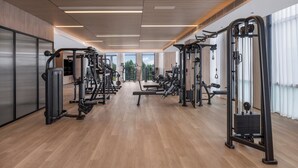 Une salle de sport moderne équipée de divers appareils d’exercice, dotée de grandes fenêtres et d’un plancher en bois.