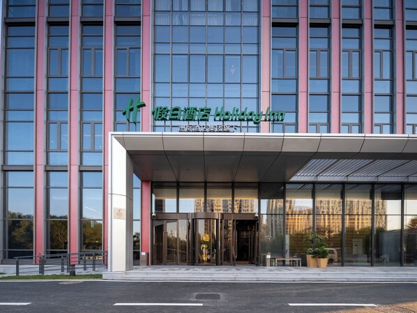 A modern hotel entrance with a glass facade, a covered entrance area, and a sign indicating it's a Holiday Inn.