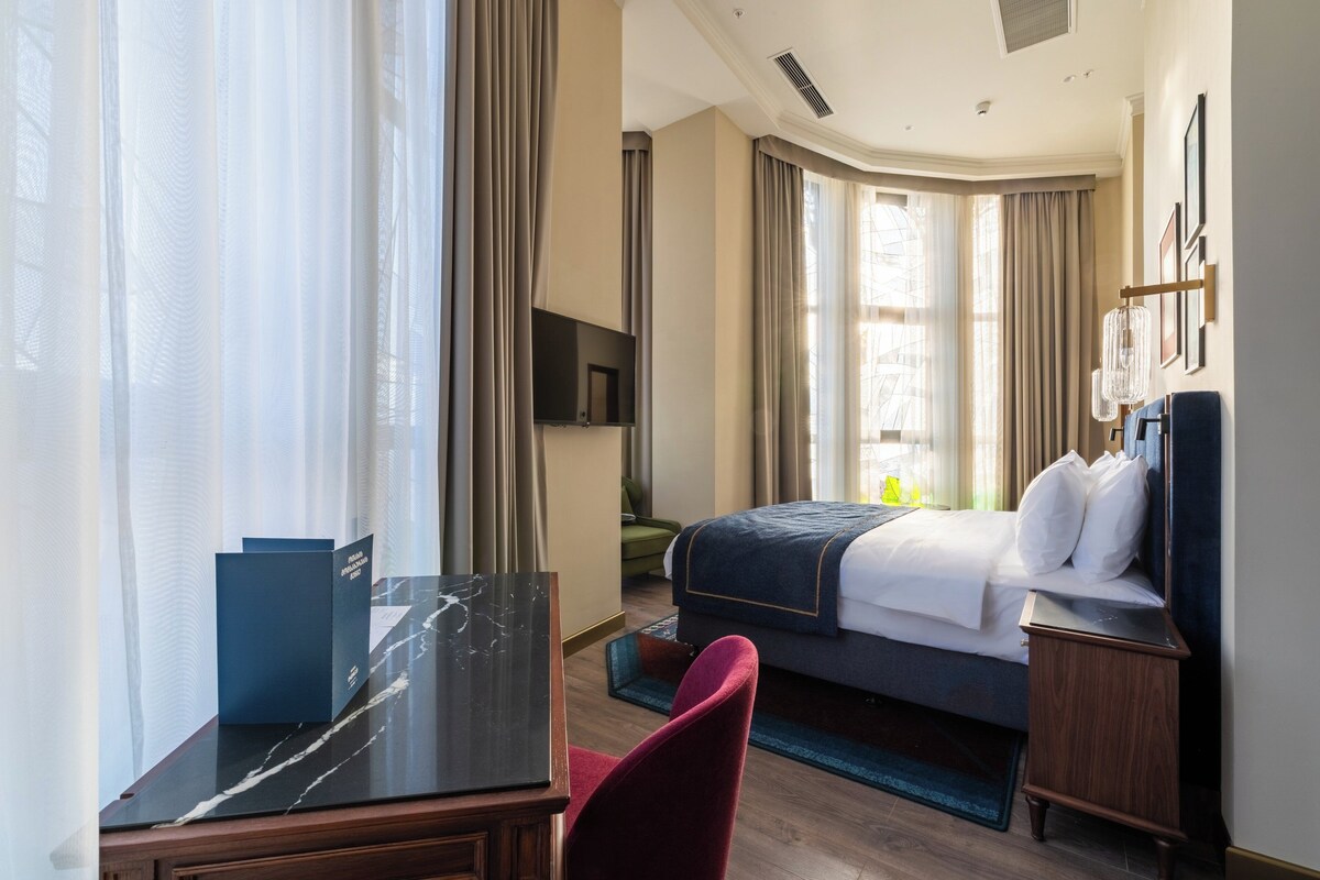 Une chambre d’hôtel avec un lit, un bureau, une chaise, une télévision et une fenêtre avec des rideaux.