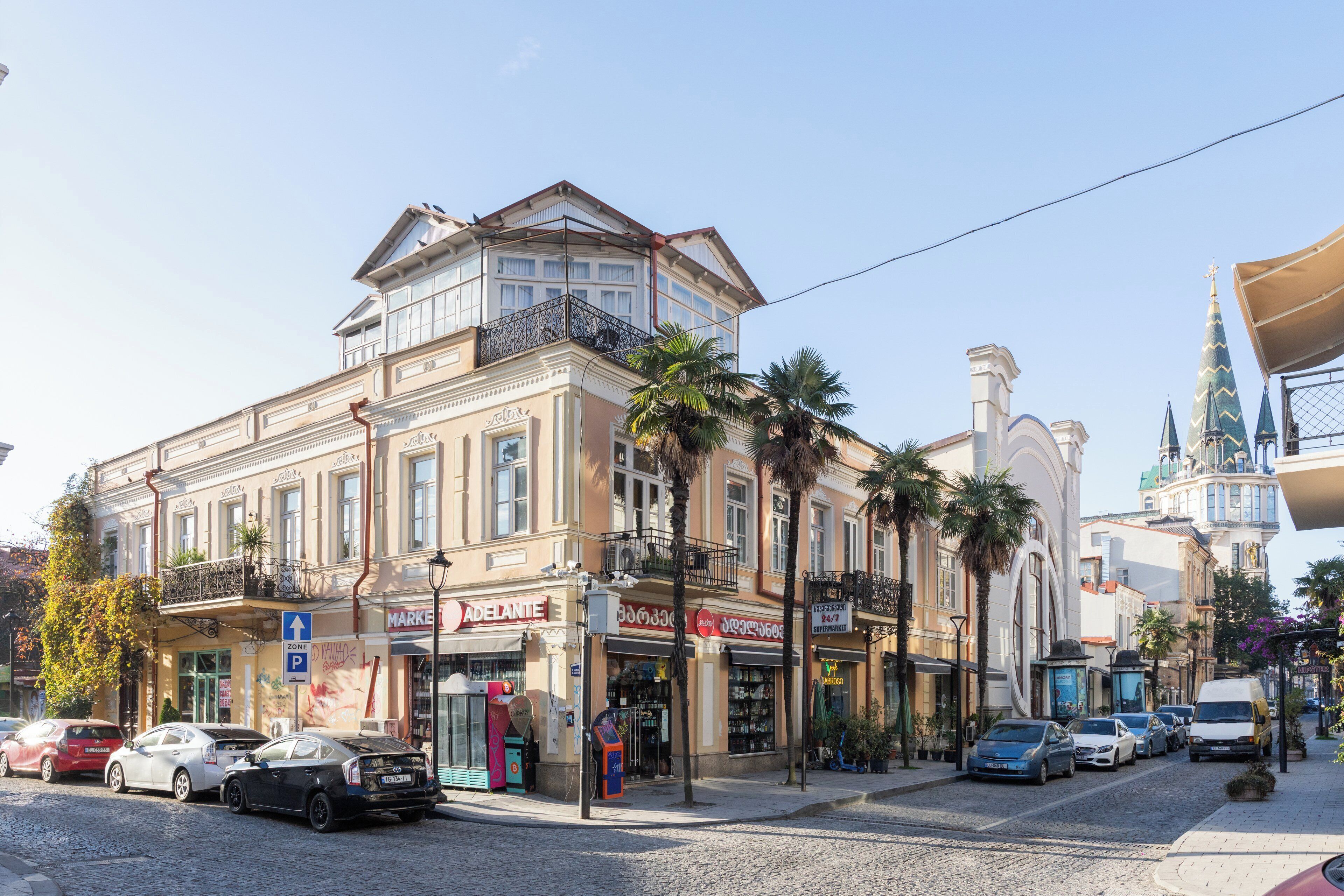 Un immeuble à plusieurs étages, doté d’une entrée d’angle bien visible, d’un balcon et d’une enseigne portant le nom « Adelante ».