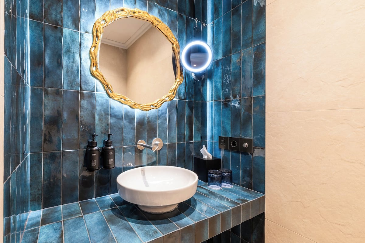 Ein Badezimmer mit einem weißen Waschbecken, einem spiegel mit goldener Rahmung und blauen Fliesen.