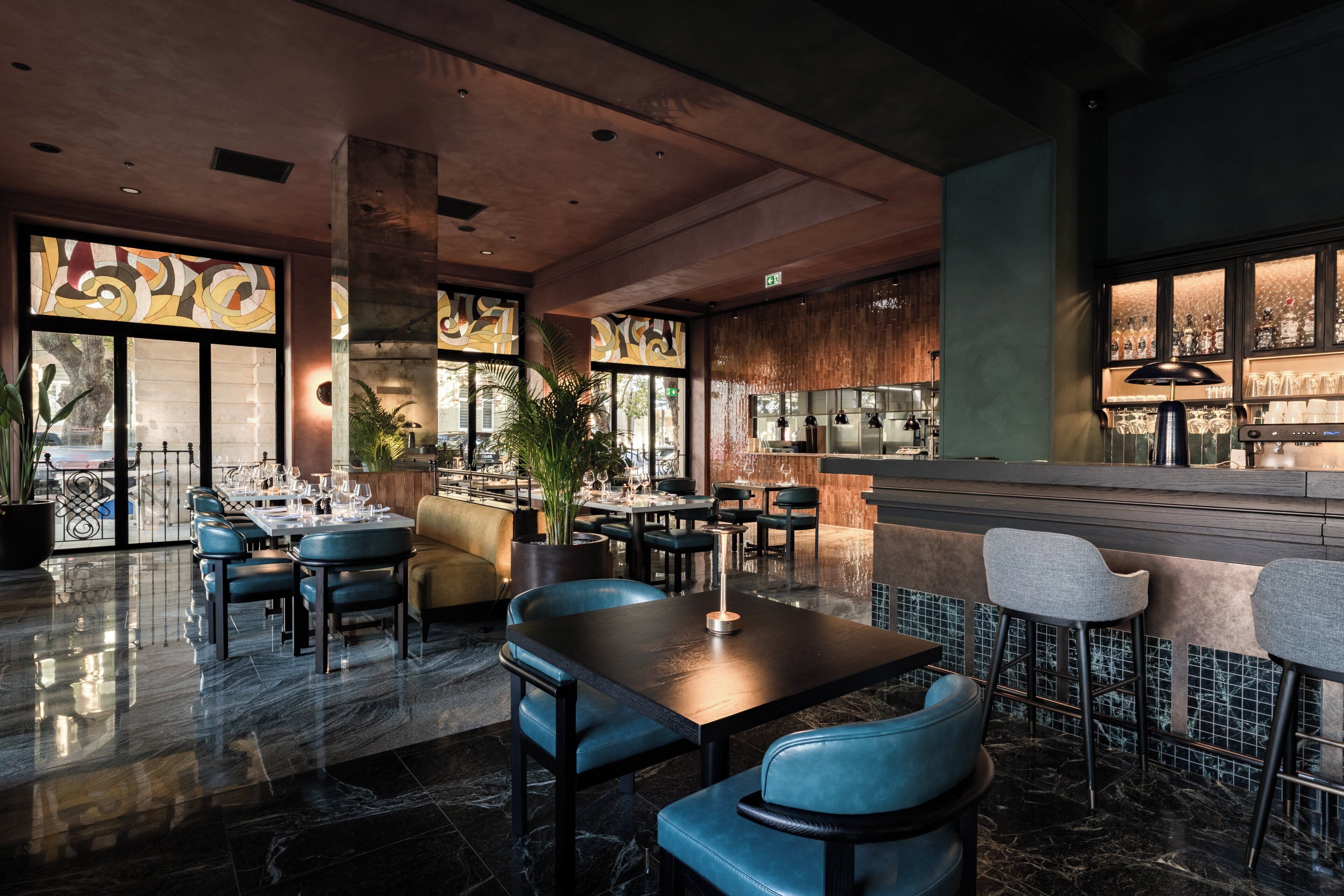 Un restaurante moderno con barra, suelo de mármol y grandes ventanales con paneles de vidrio decorativos.