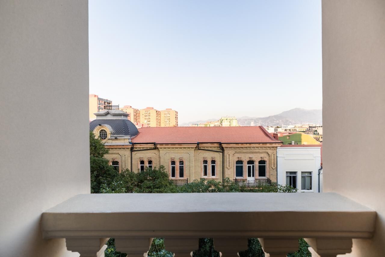 A balcony with a view of a building with a red roof and arched windows.