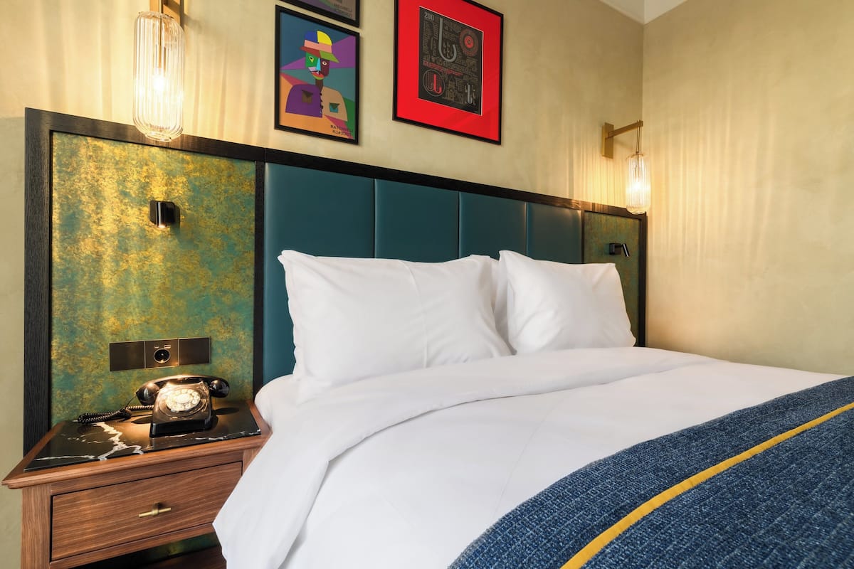 Ein Hotelzimmer mit einem Bett, einem Nachttisch mit Wählscheibentelefon und Wandbildern.