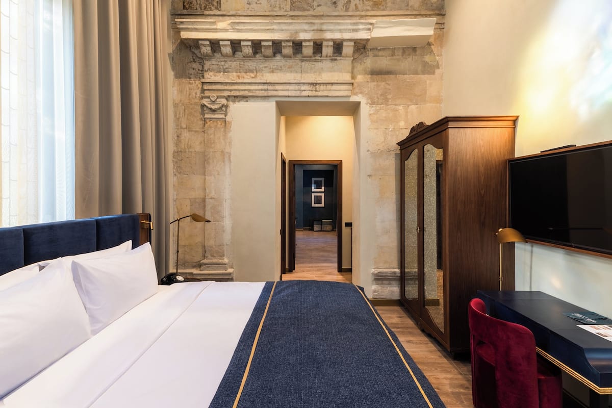 Ein Hotelzimmer mit einem großen Bett, einem Schreibtisch mit Stuhl, einem Fernseher und einem Spiegel.