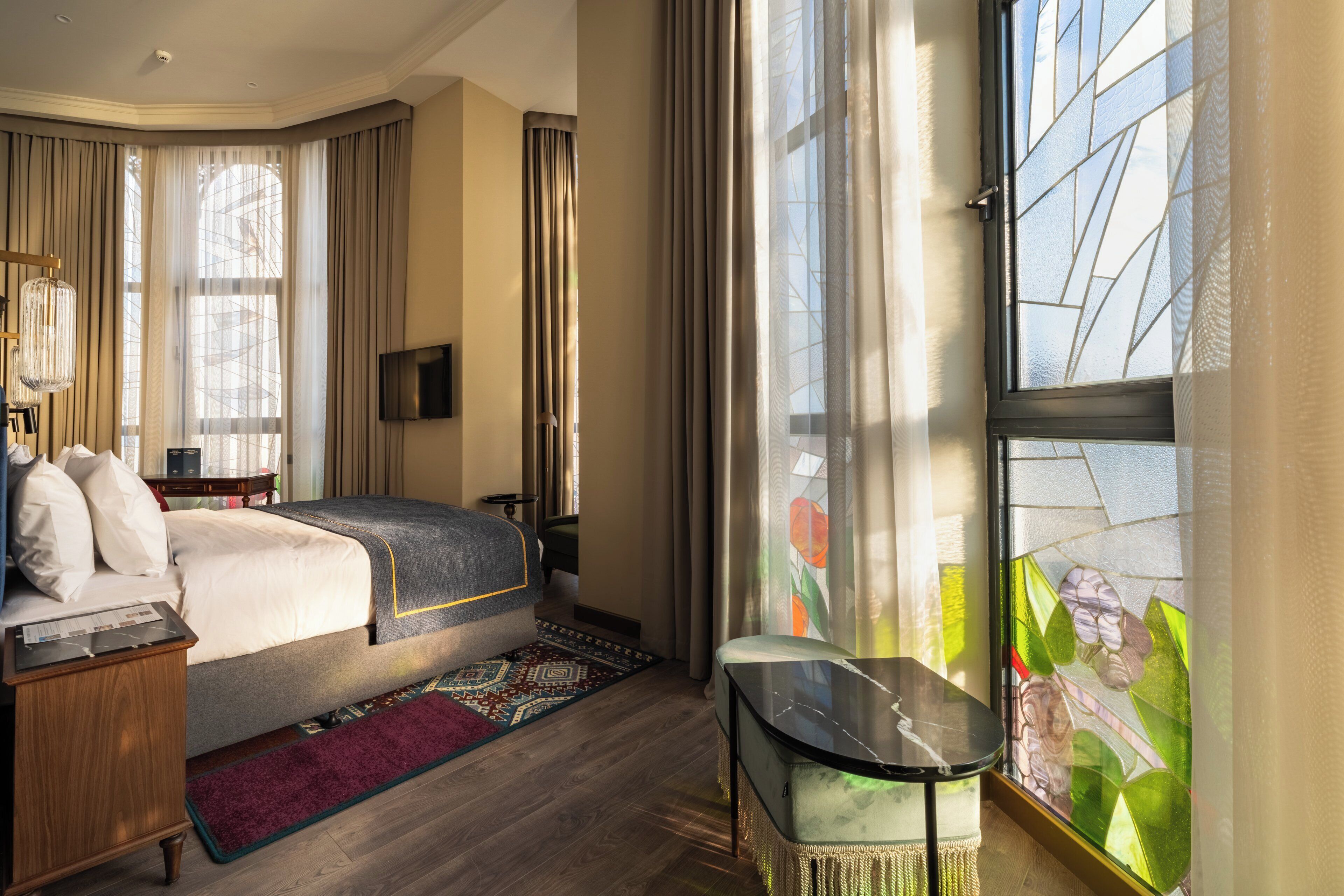 Una habitación de hotel con cama, escritorio, televisor y un ventanal con cortinas.