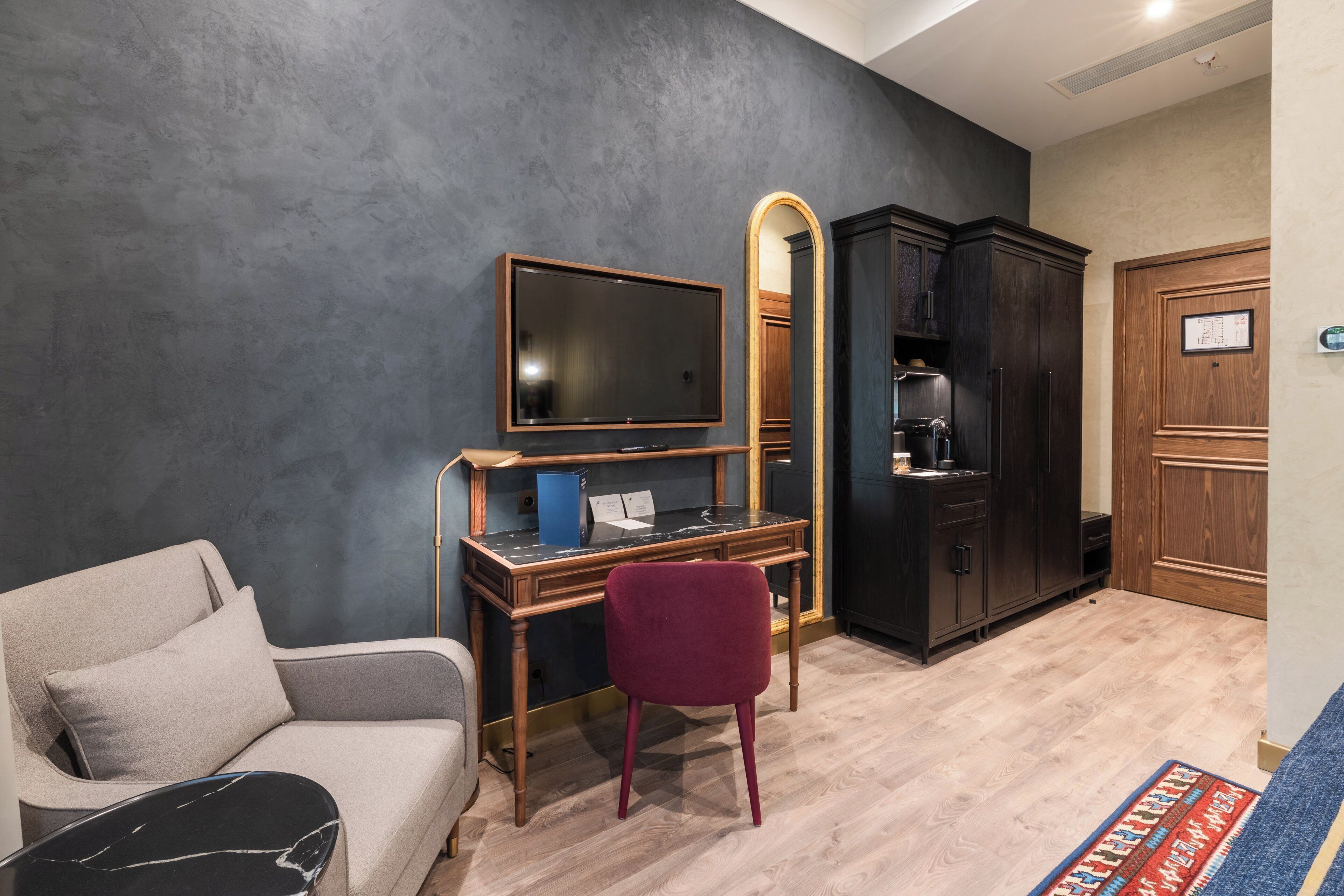 Una habitación con sofá, escritorio con ordenador, televisor, espejo y armario.