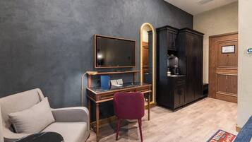 Una habitación con sofá, escritorio con ordenador, televisor, espejo y armario.