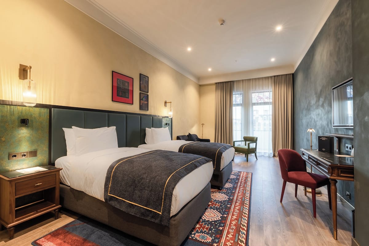 Ein Hotelzimmer mit zwei Betten, einem Schreibtisch, einem Sessel und einem Fernseher.