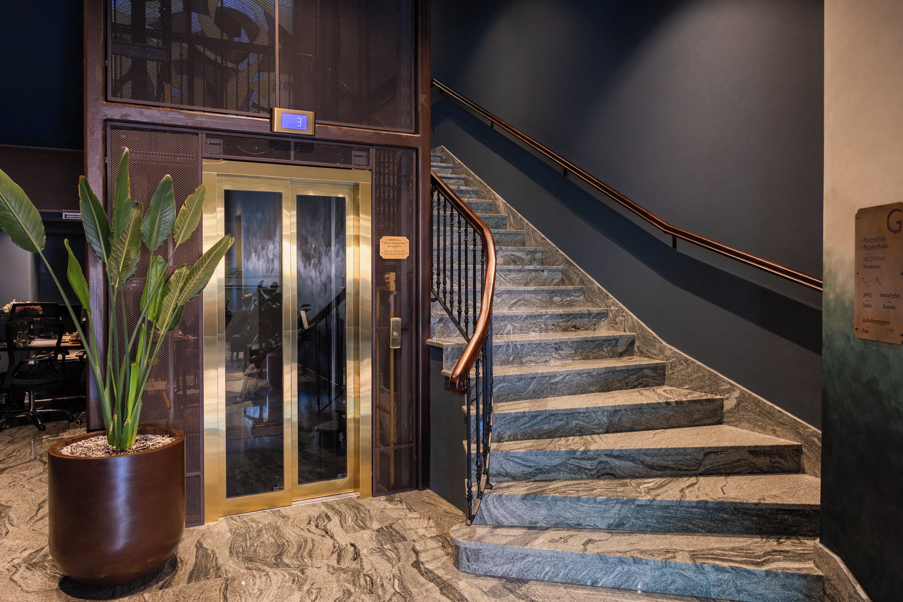 A marble staircase with a metal railing leading to an elevator.