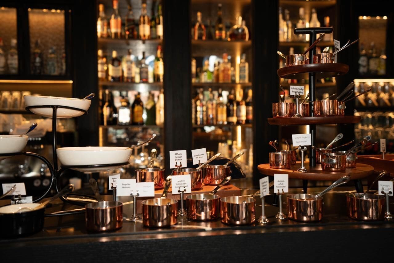 A bar area with multiple copper serving dishes and utensils, with a background of shelves stocked with various bottles.