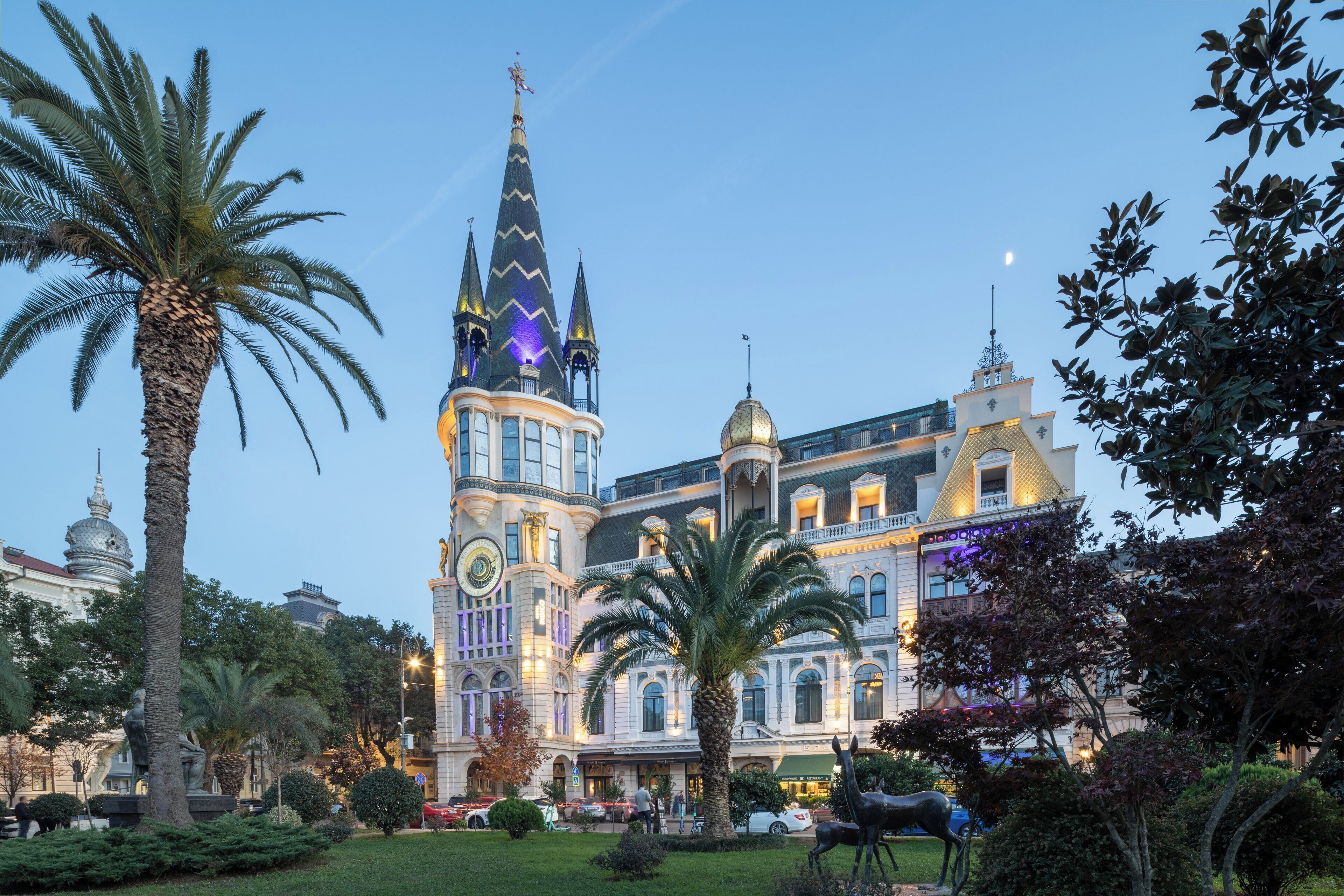 A large, ornate building with multiple spires and domes, surrounded by lush greenery and palm trees.