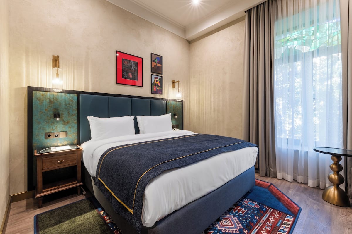 Ein Hotelzimmer mit einem großen Bett, einem Nachttisch, einer Wandlampe und einem Fenster mit Vorhängen.