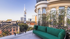 Ein Balkon mit einem grünen Sofa, einem schmiedeeisernen Geländer und Blick auf einen modernen Wolkenkratzer.