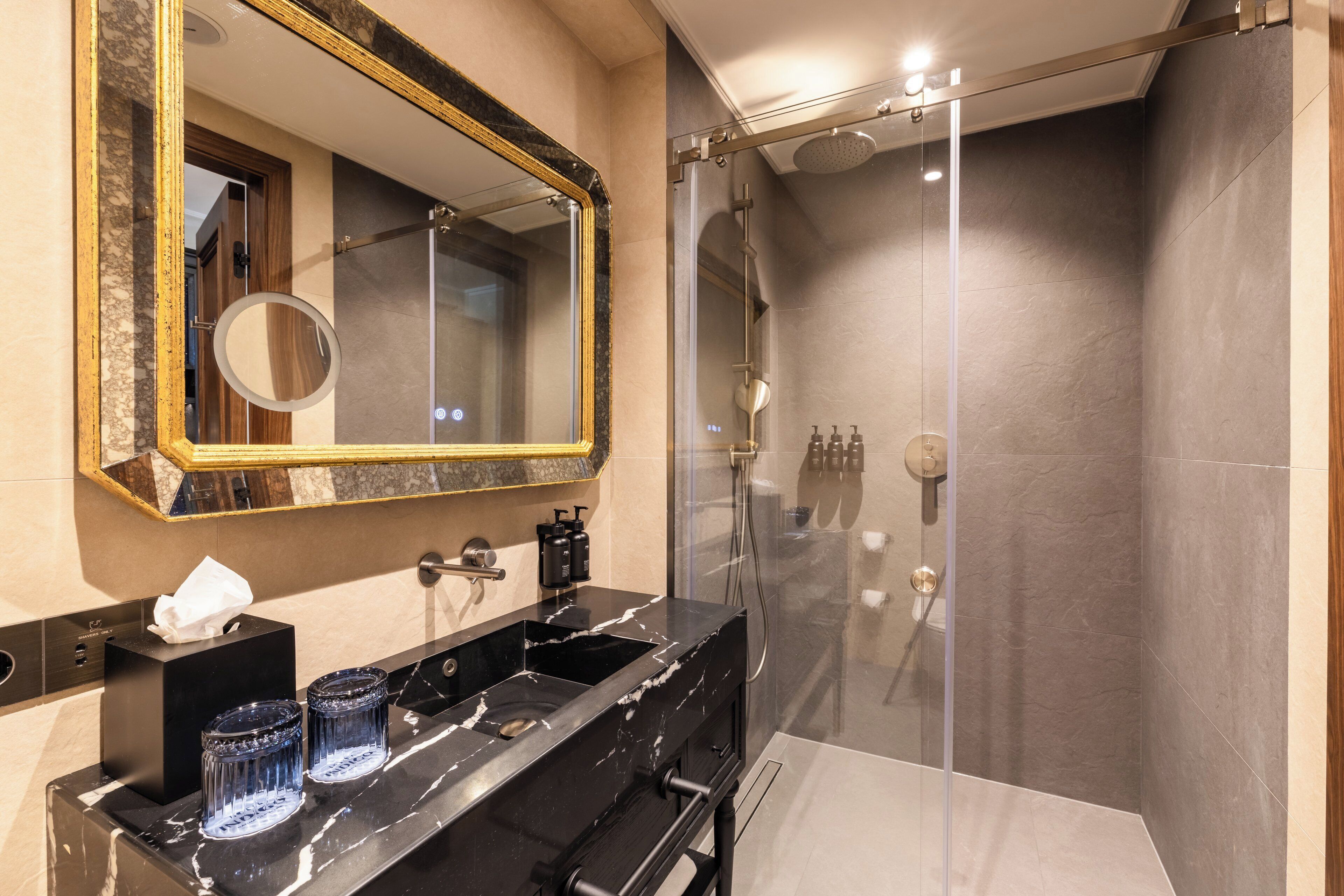 A modern bathroom with a large mirror, a black marble sink, and a glass-enclosed shower.