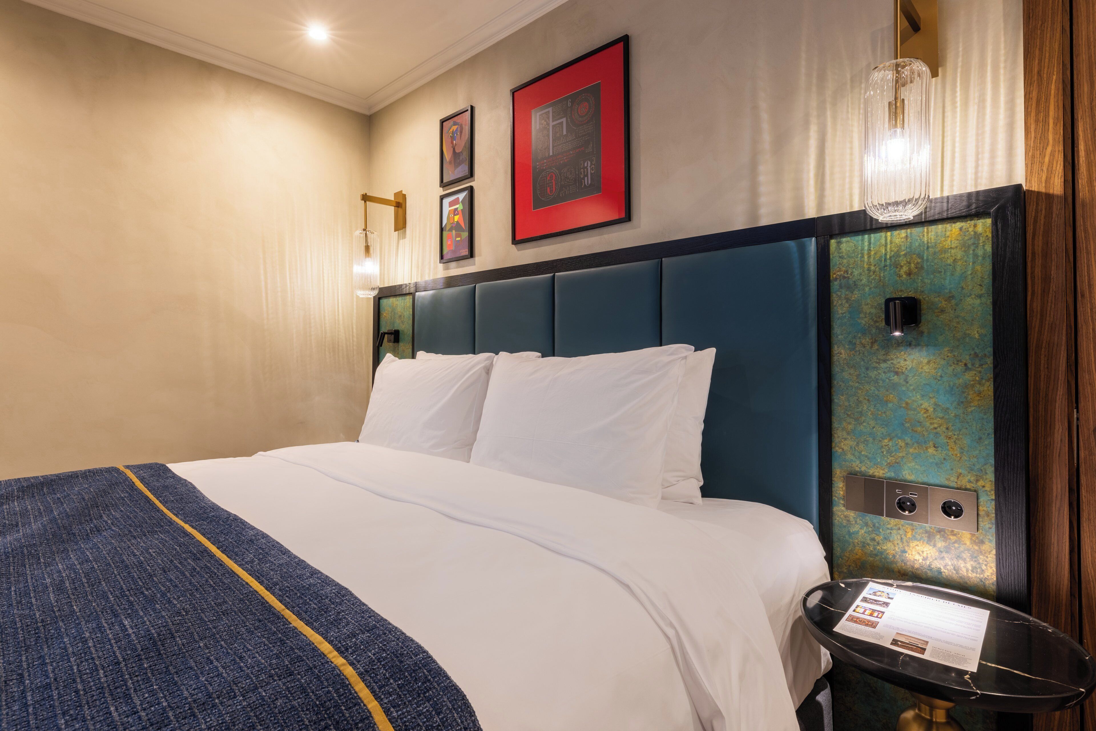 A hotel room with a large bed, a bedside table, and a wall-mounted control panel.