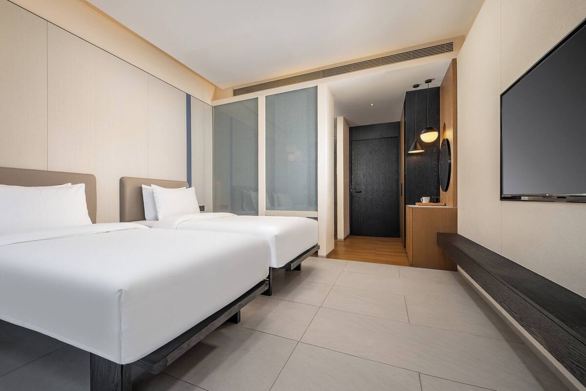 Ein Hotelzimmer mit zwei Betten, einem großen Spiegel, einem Flachbildfernseher und einer hölzernen Bank.