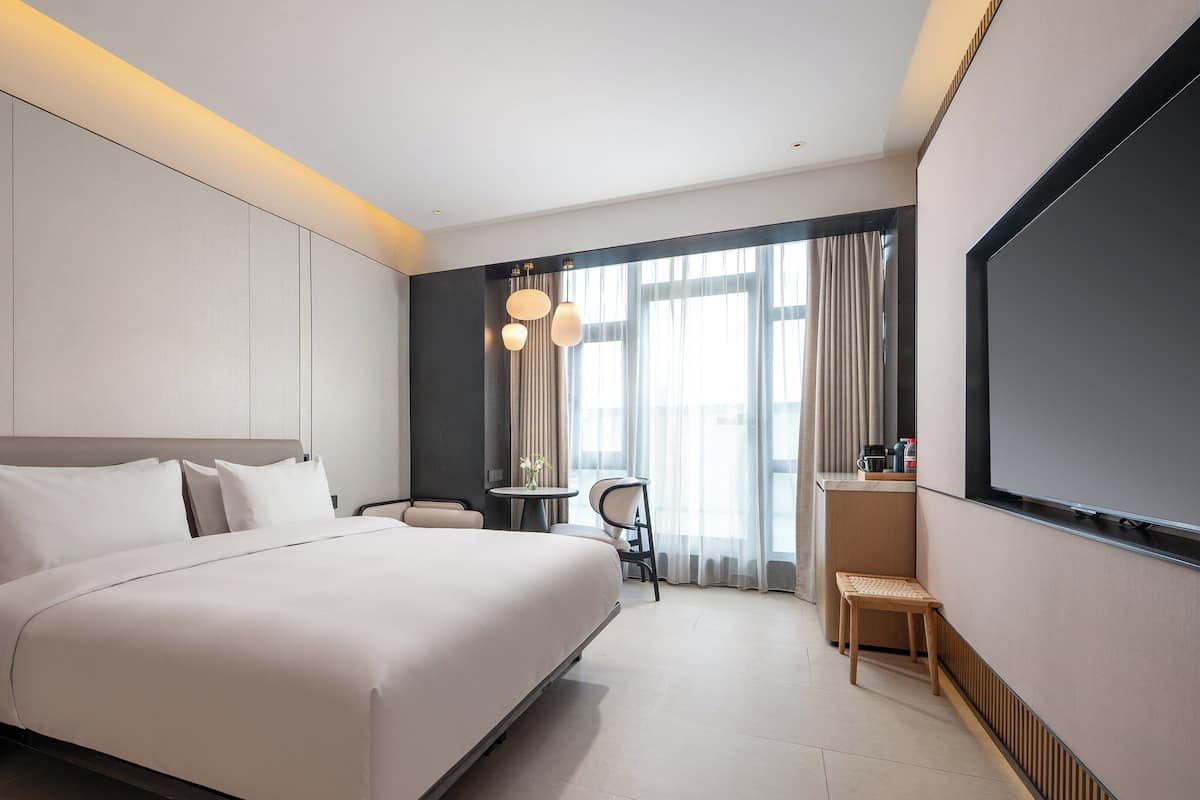 Ein modernes Hotelzimmer mit einem großen Bett, einem kleinen Tisch, einem Sessel und einem Fernseher.