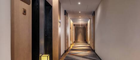 A long, narrow hotel corridor with wooden walls, a patterned carpet, and a small table lamp.