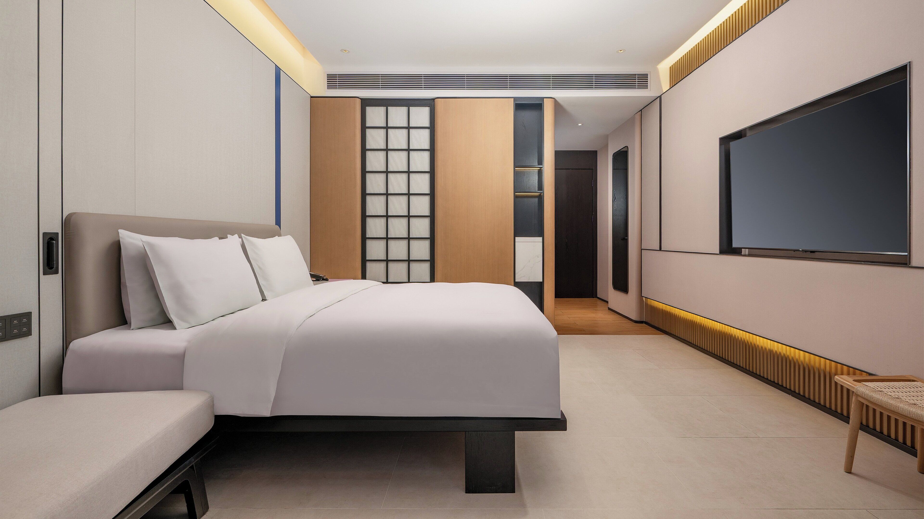 A modern hotel room with a large bed, a TV, and a walk-in closet.