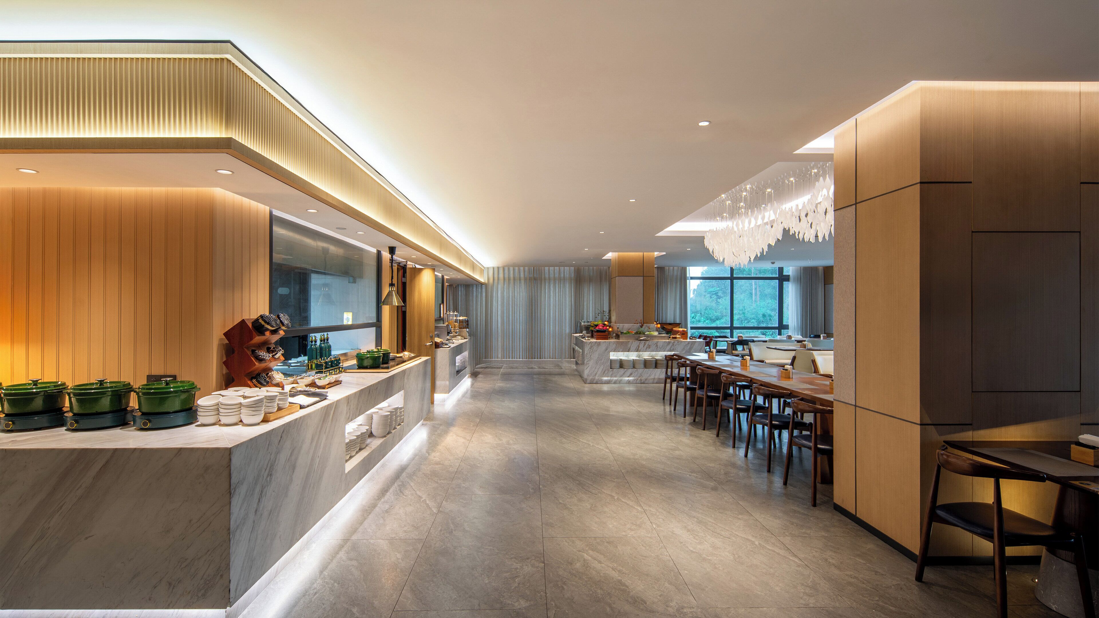 A modern kitchen with a marble countertop, wooden cabinets, and a large window providing a view of the outdoors.