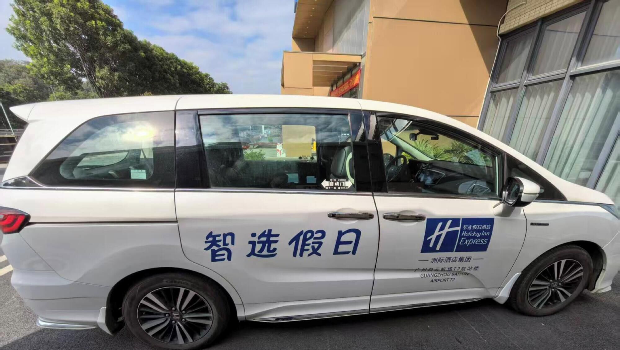 Una camioneta blanca con texto y logotipos azules, estacionada frente a un edificio con un gran ventanal.