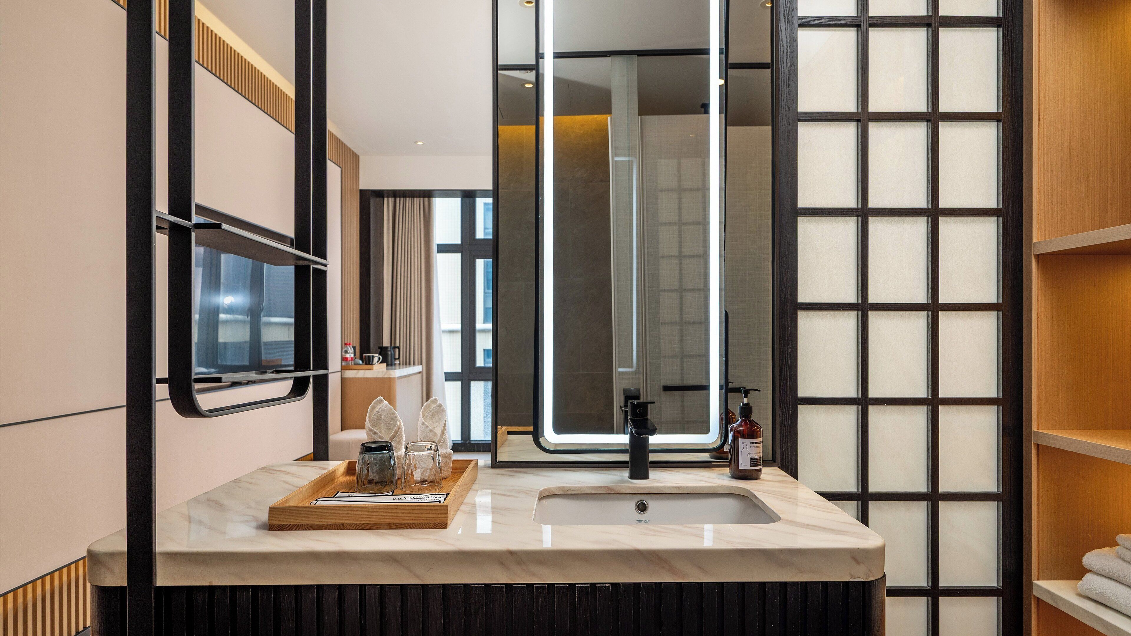 Un baño moderno con un espejo grande, un lavabo y una bandeja de madera con cristalería.