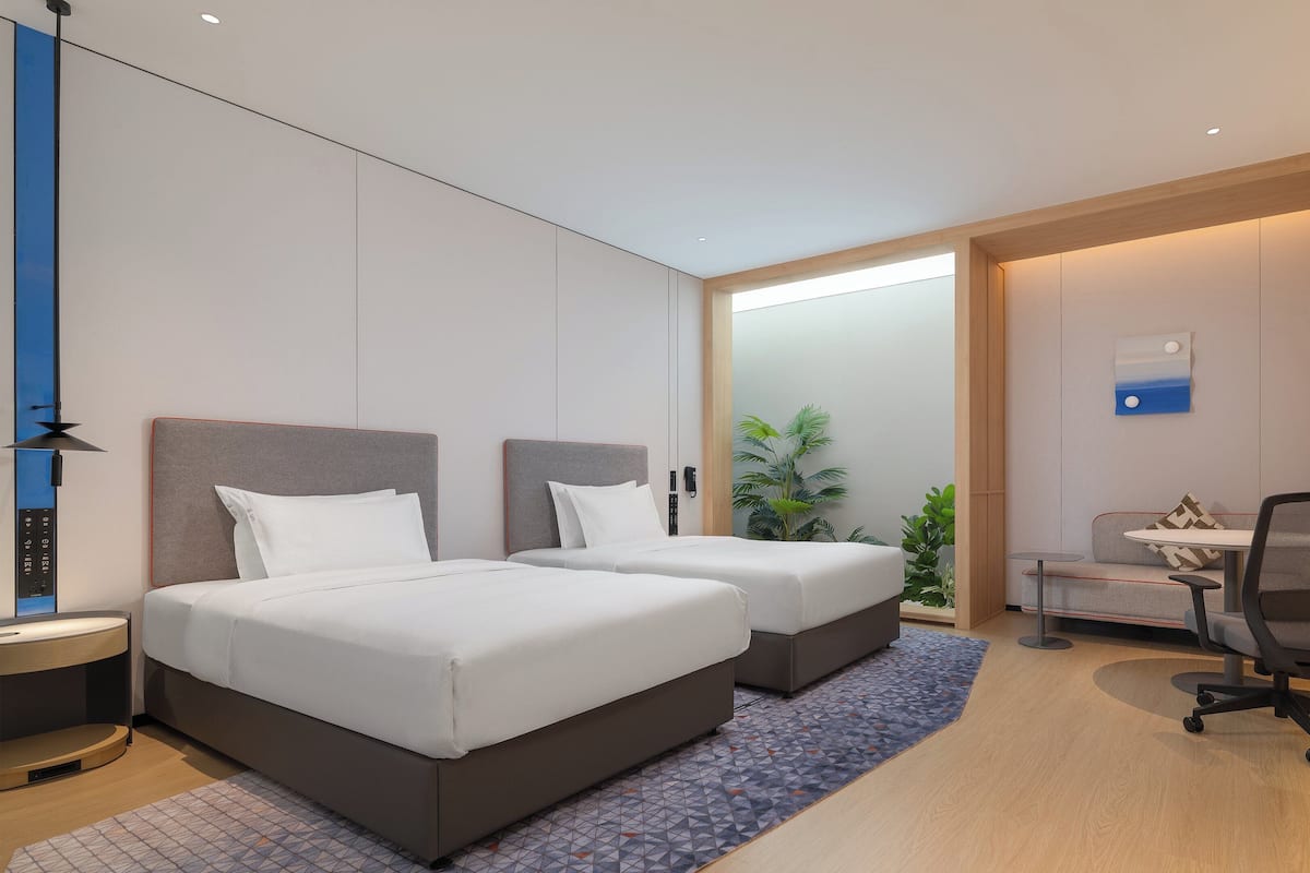 Une chambre d’hôtel moderne équipée de deux lits, d’un bureau, d’une chaise, d’une télévision et d’une plante.