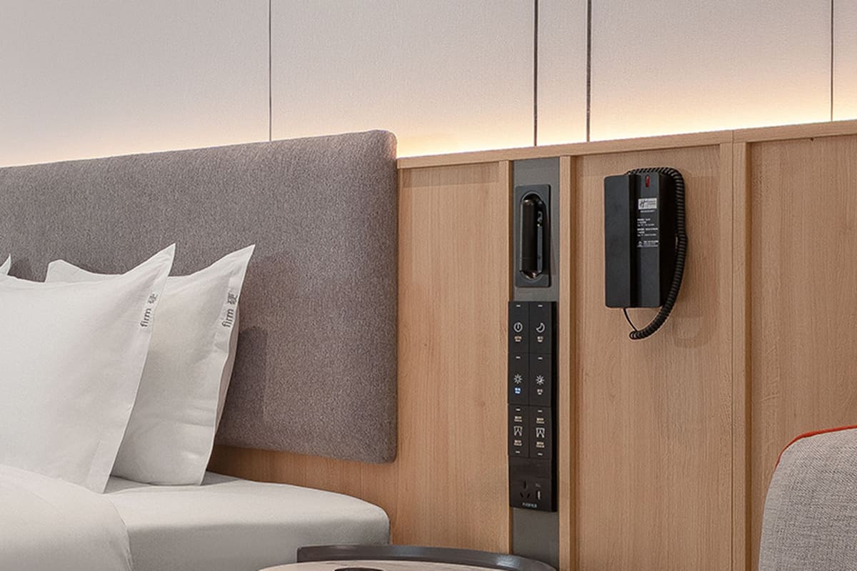 Une chambre d’hôtel équipée d’un lit, d’oreillers, d’un panneau de commande et d’un téléphone.
