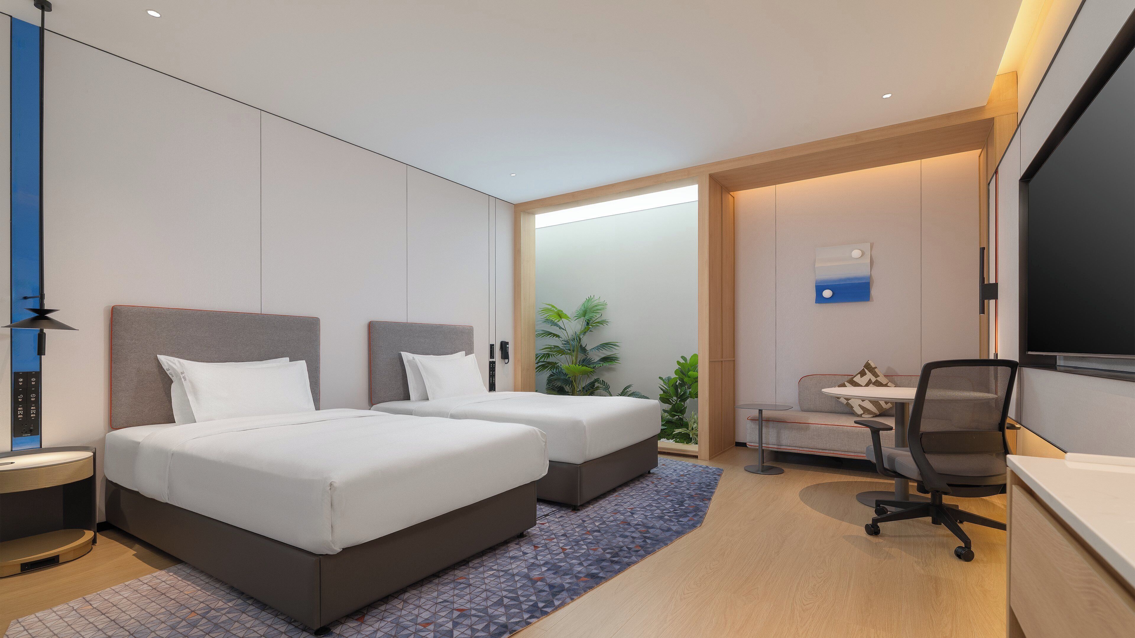A modern hotel room with two beds, a desk, a chair, a TV, and a plant.