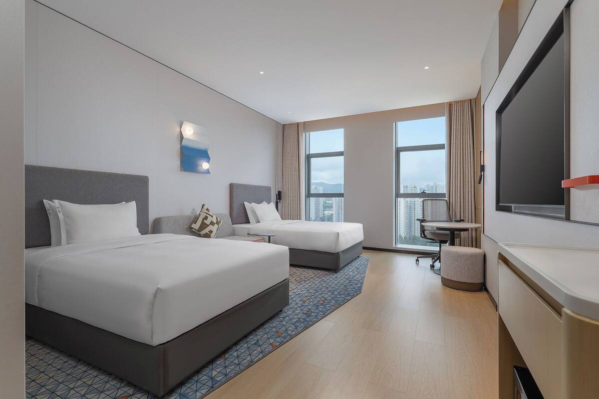 Une chambre d’hôtel avec deux lits, un bureau, une télévision et une grande fenêtre donnant sur la ville.