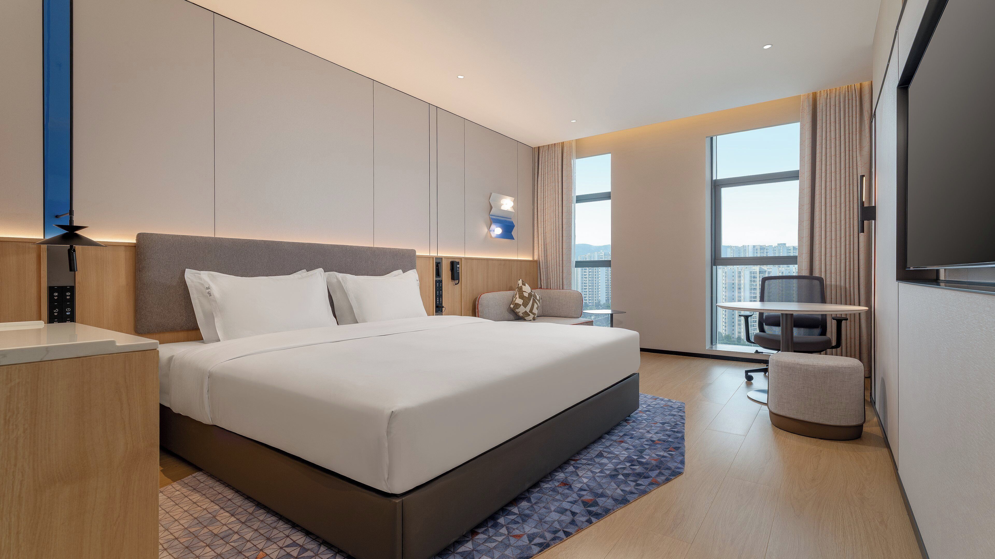 Ein modernes Hotelzimmer mit einem großen Bett, einem Schreibtisch, einem Sessel und einem Fernseher.