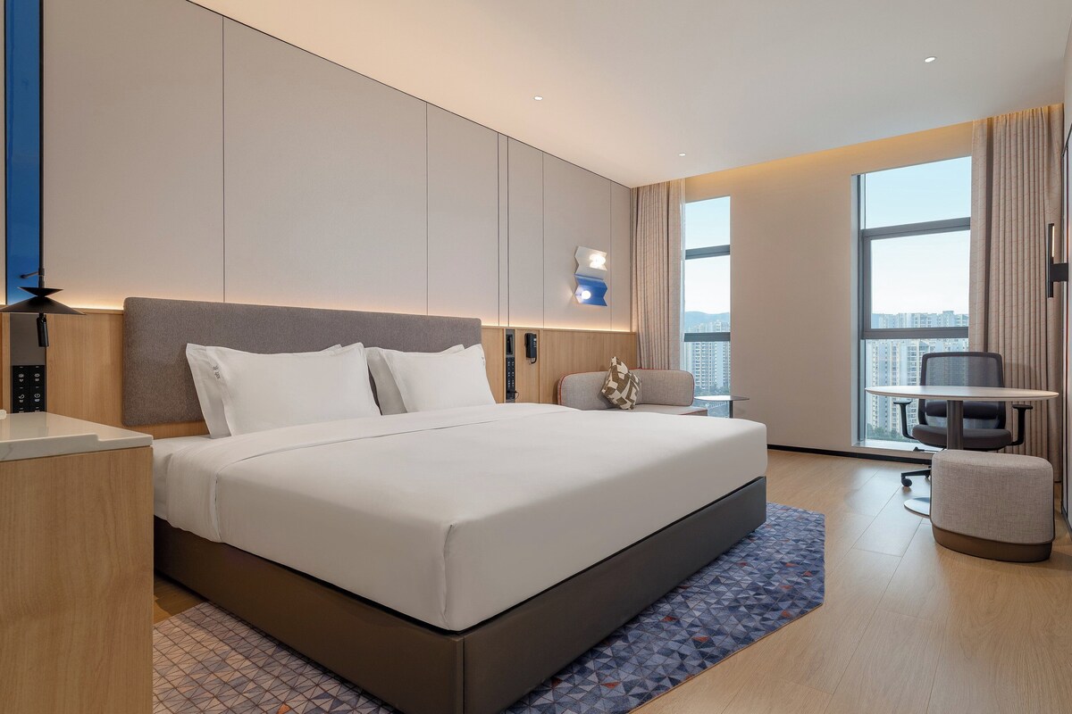 A modern hotel room with a large bed, a desk, a chair, and a TV.