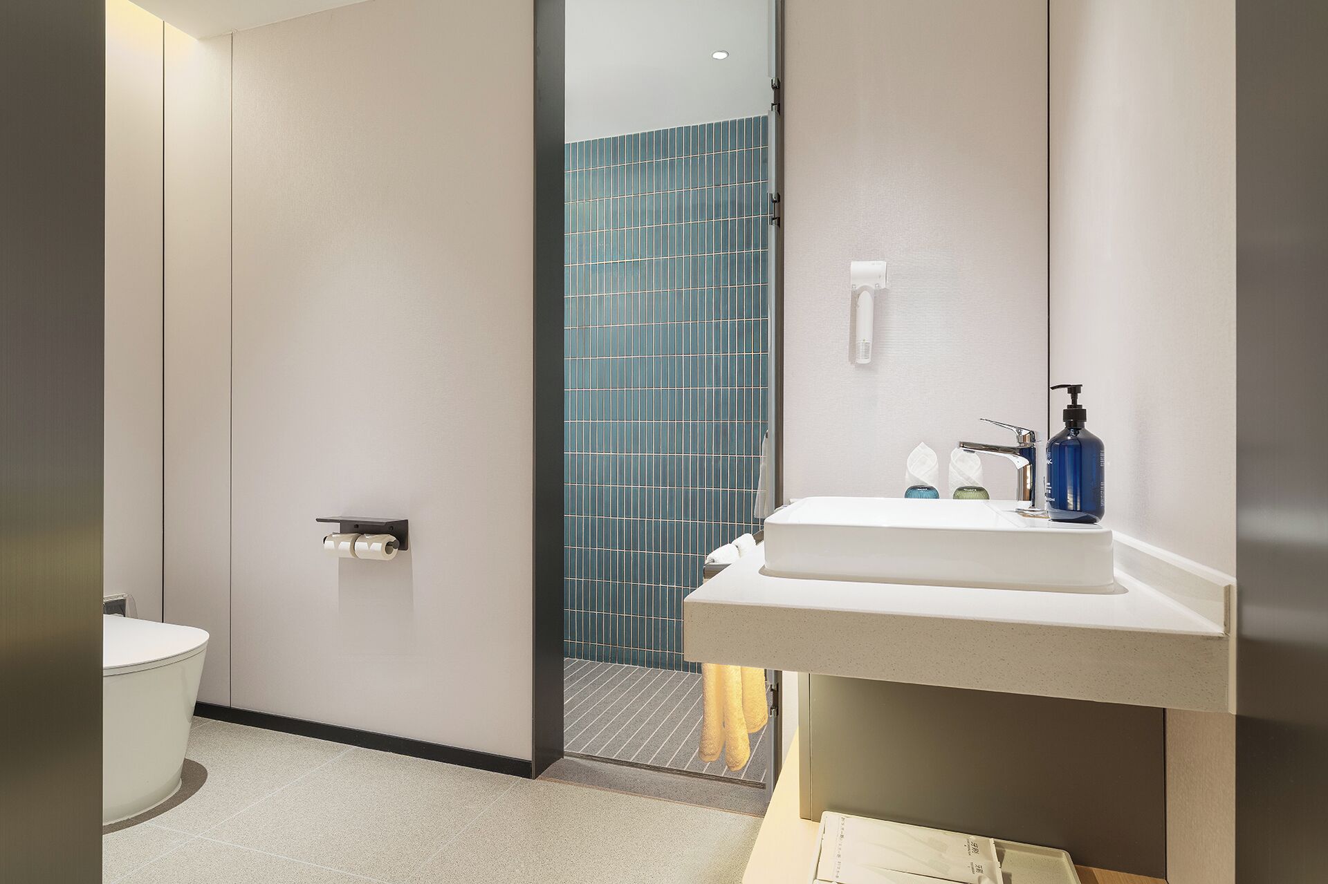 Une salle de bain moderne avec un lavabo blanc, un miroir et une zone de douche carrelée de bleu.