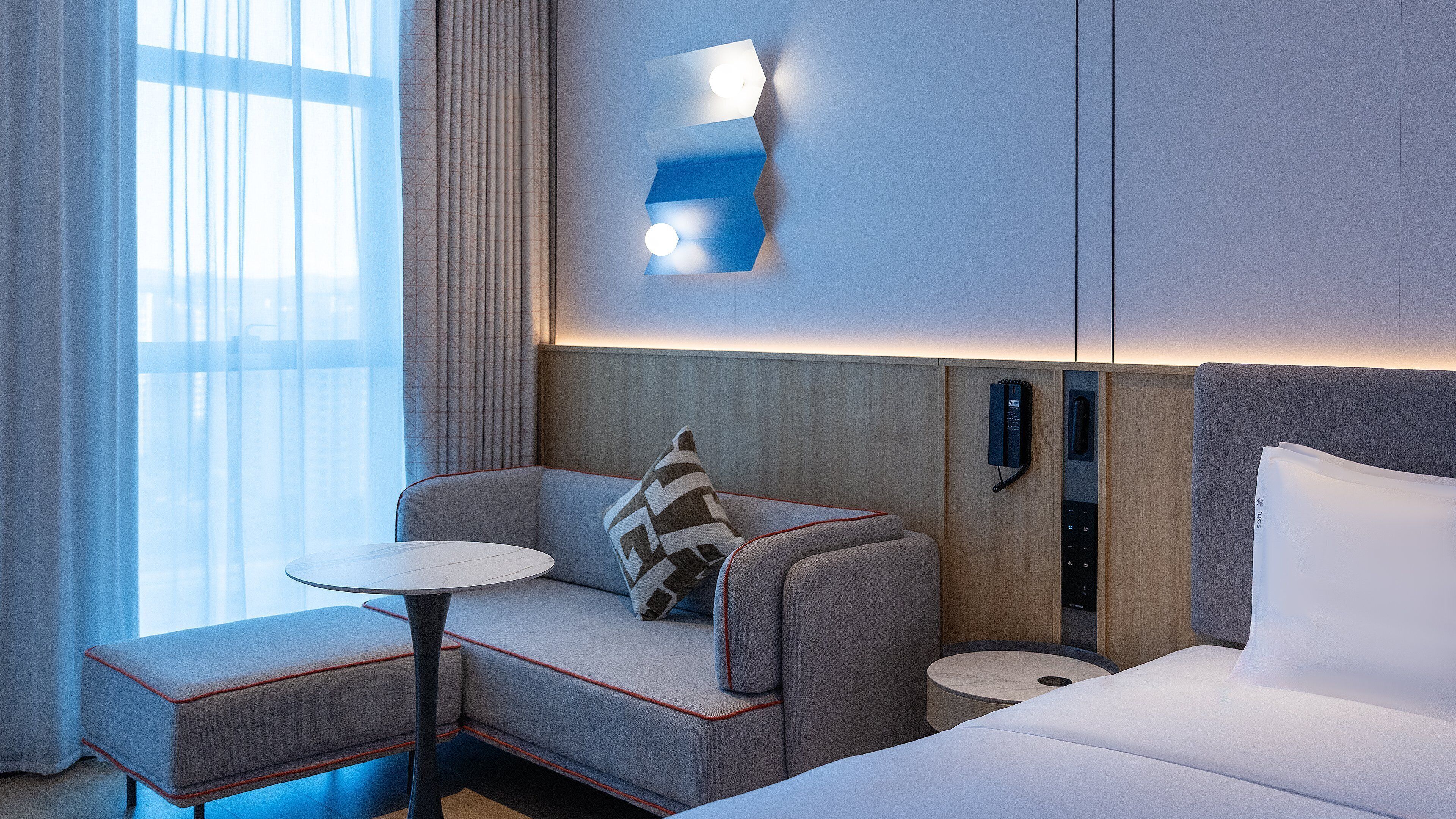 Habitación de hotel con sofá, una mesita, cama y lámpara fijada a la pared.