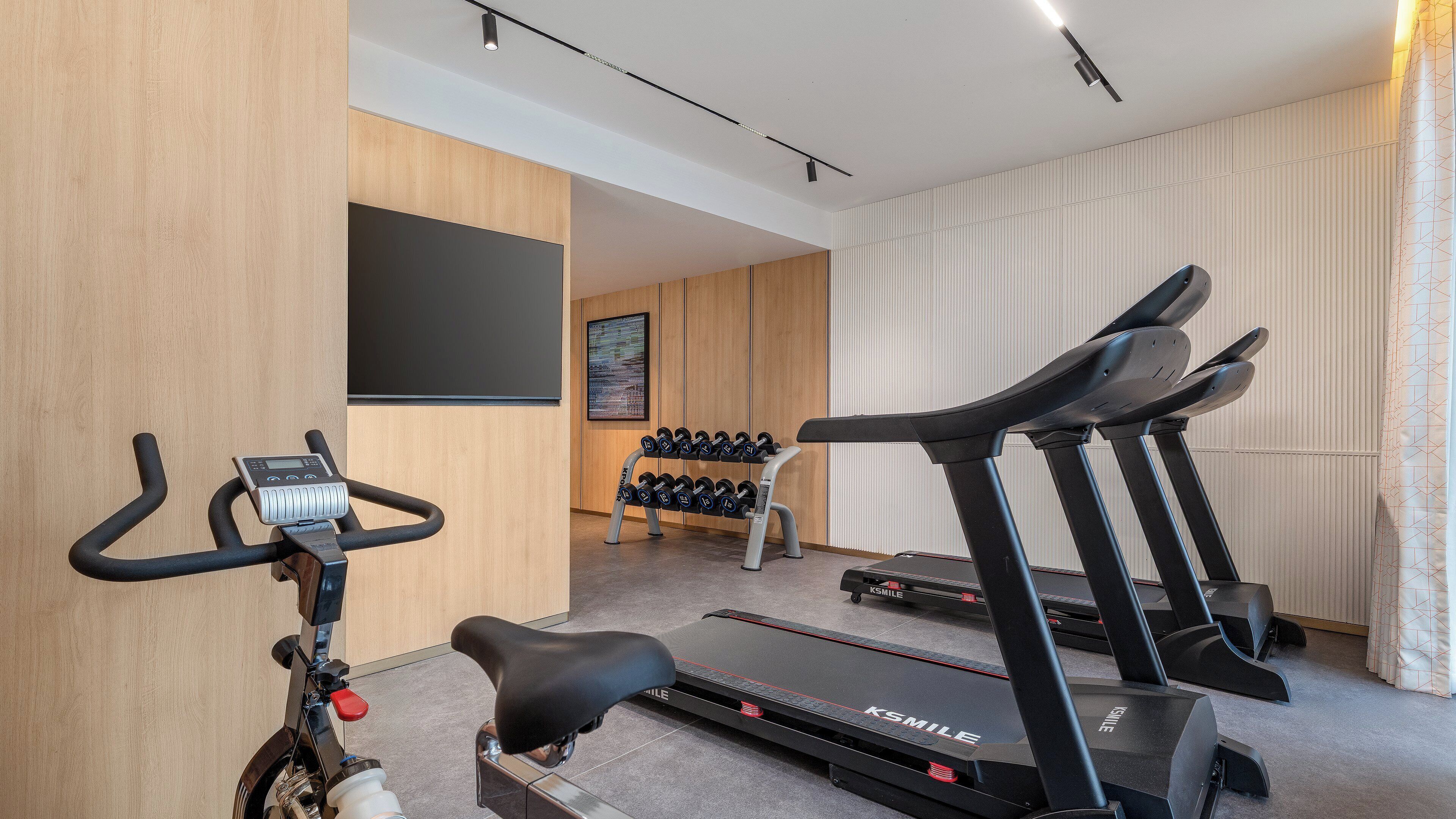 Un gimnasio en casa con una bicicleta estática, cinta de correr y mancuernas.