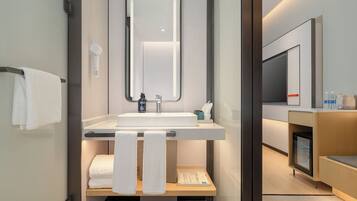 Un baño moderno con lavabo, espejo, toallero y un estante con artículos de aseo.